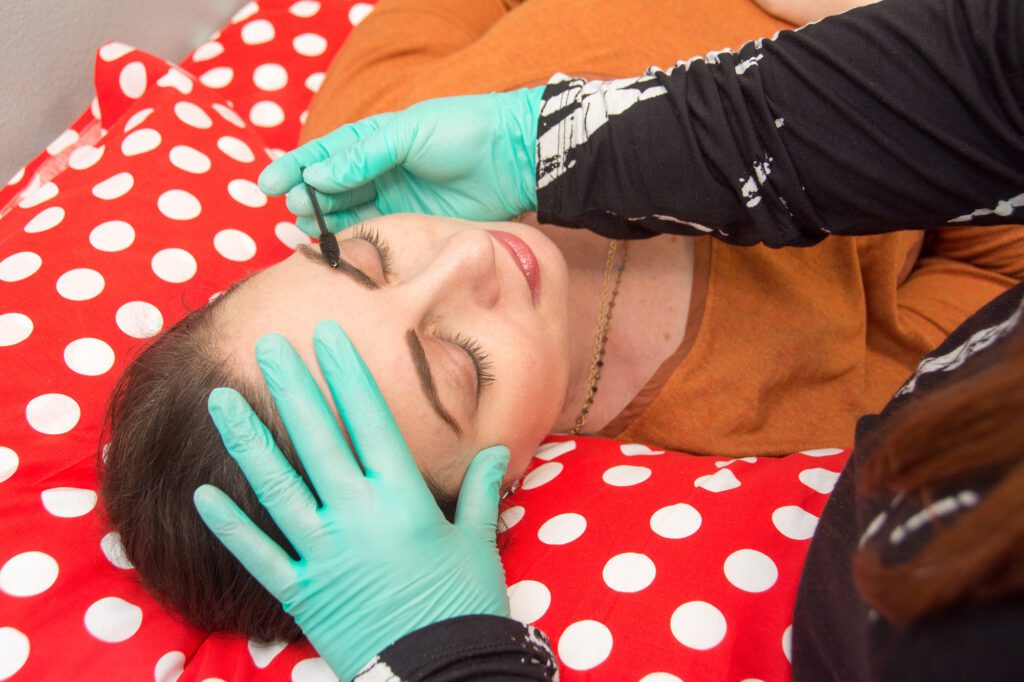 Fair-skinned woman in an orange blouse getting her eyebrows done