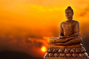 Brown statue of a meditating buddha with a sunset in the background