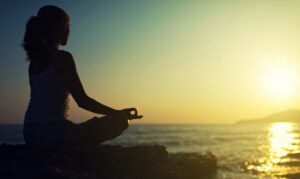 Silhouette of a woman meditating in front of a sunrise